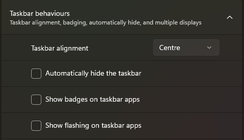 A screenshot from Windows 11 settings: Title: Taskbar behaviours Subtitle: Taskbar alignment, badging, automatically hide, and multiple displays. Options: Taskbar alignment (set to Centre) Automatically hide the taskbar (unchecked) Show badges on taskbar apps (unchecked) Show flashing on taskbar apps (unchecked)